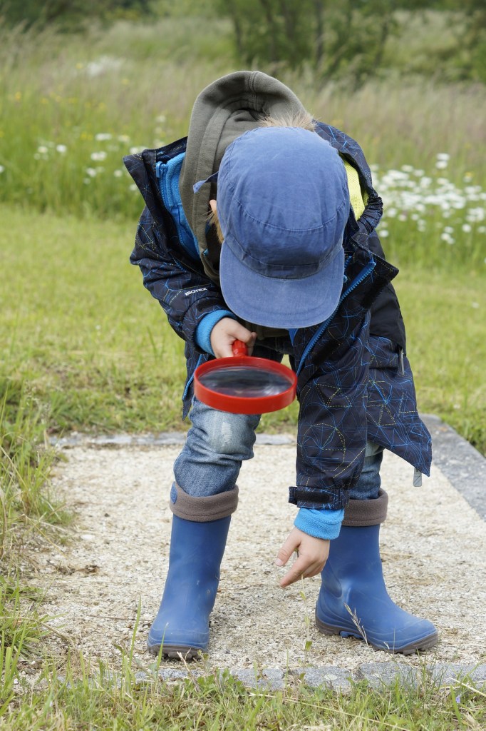 Child with magnifying glass looking down at the ground.